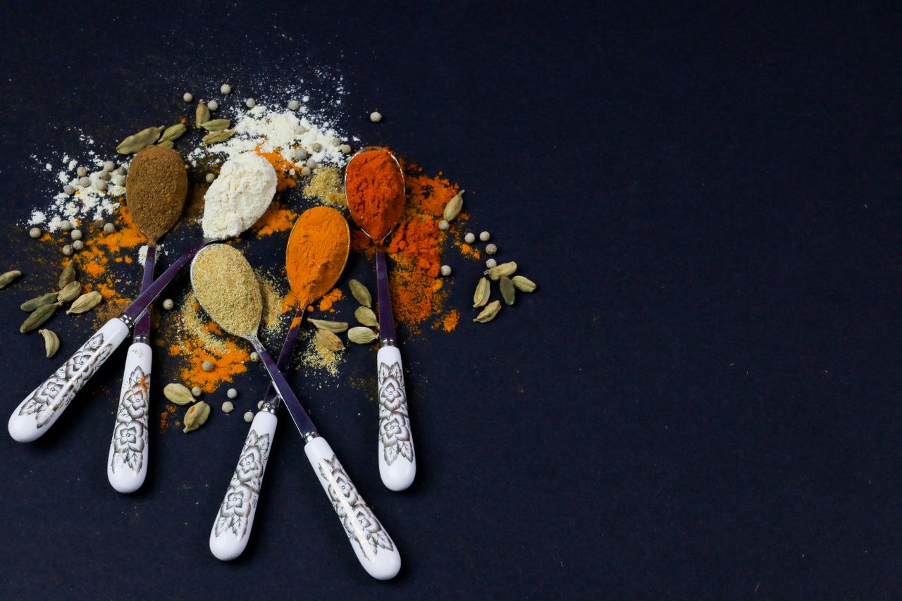 An artistic arrangement of colorful spices on elegant spoons with a dark background.
